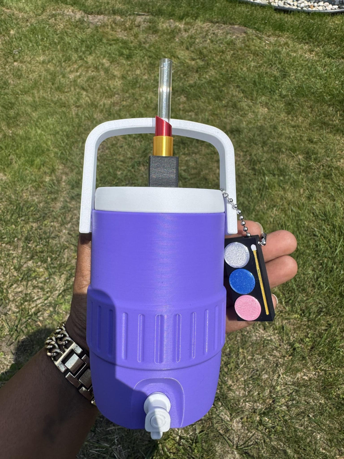 May include: A purple beverage cooler with a white handle and lid, featuring a metallic topper and a small black nail saver can opener attached by a chain. The text SECURE THE SET COOLER + TOPPER + NAIL SAVER CAN OPENER BUNDLE and BE LIK3 are visible.